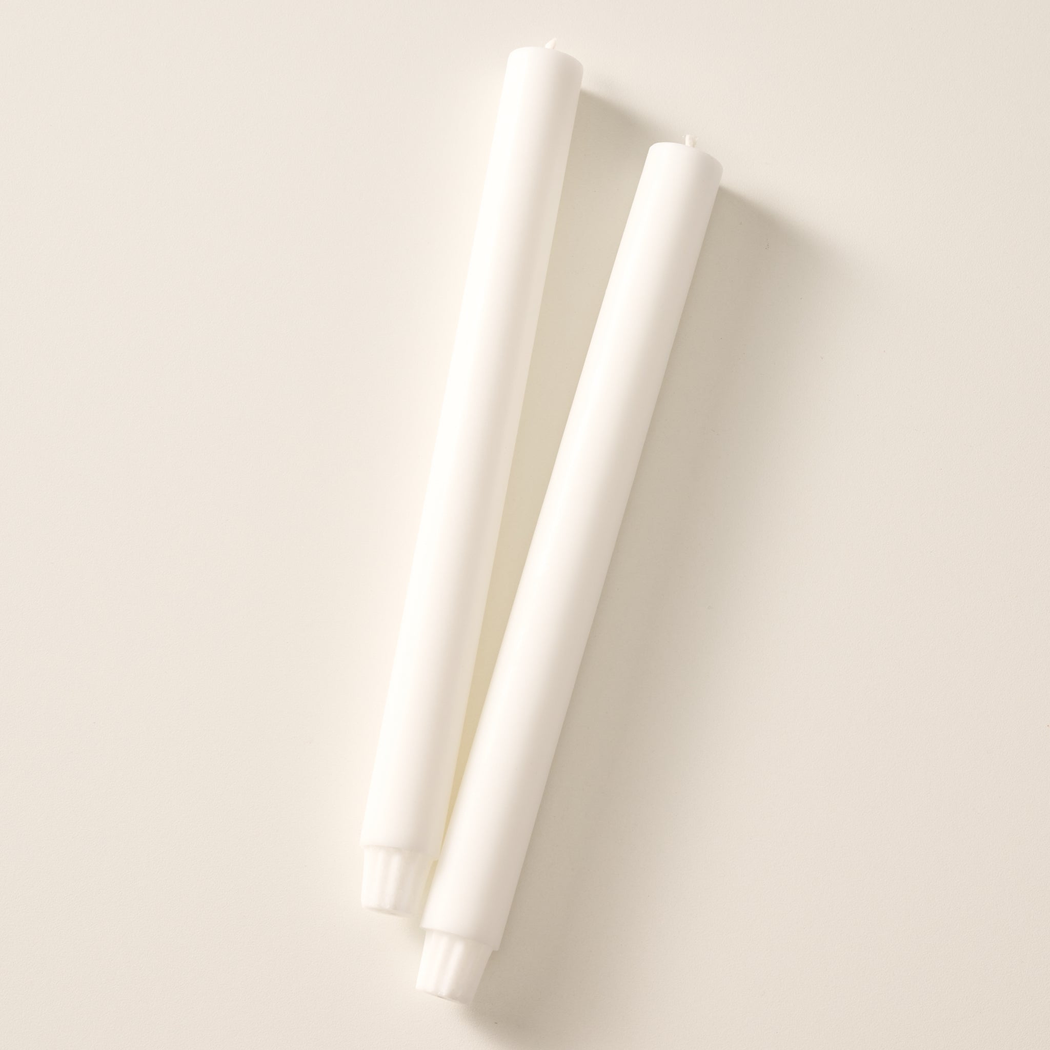 Two natural white colored pillar candles with ribbed bases, laying flat on a white background.