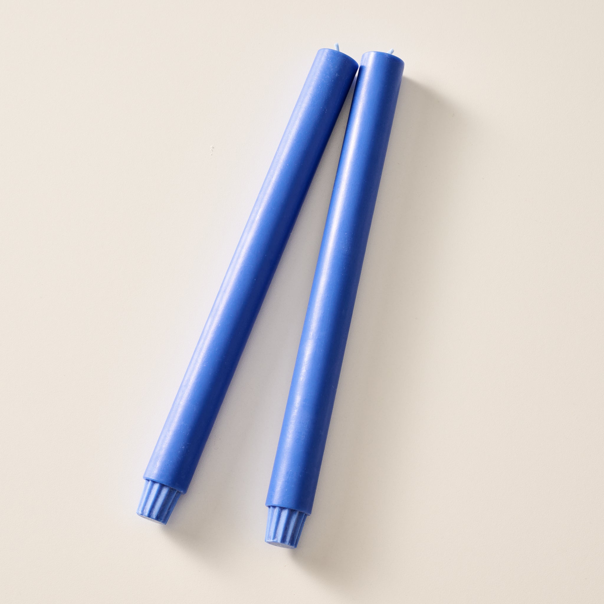 Two cobalt blue pillar candles with ribbed bases, laying flat on a white background.