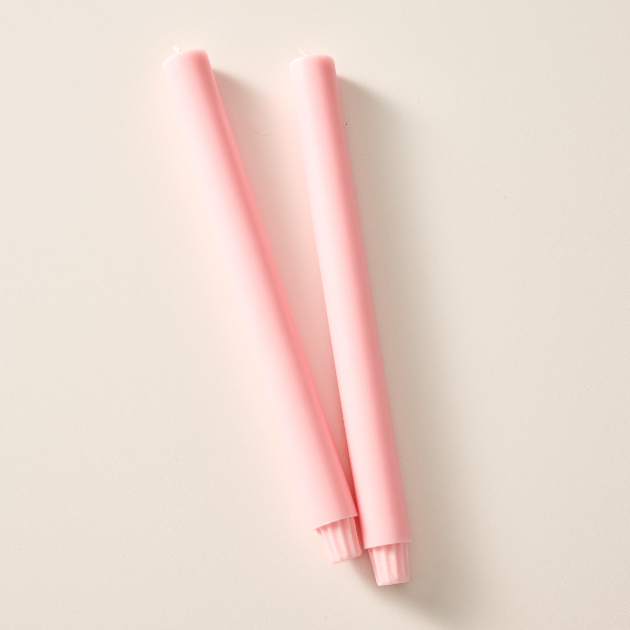 Two ginger pink colored pillar candles with ribbed bases, laying flat on a white background.