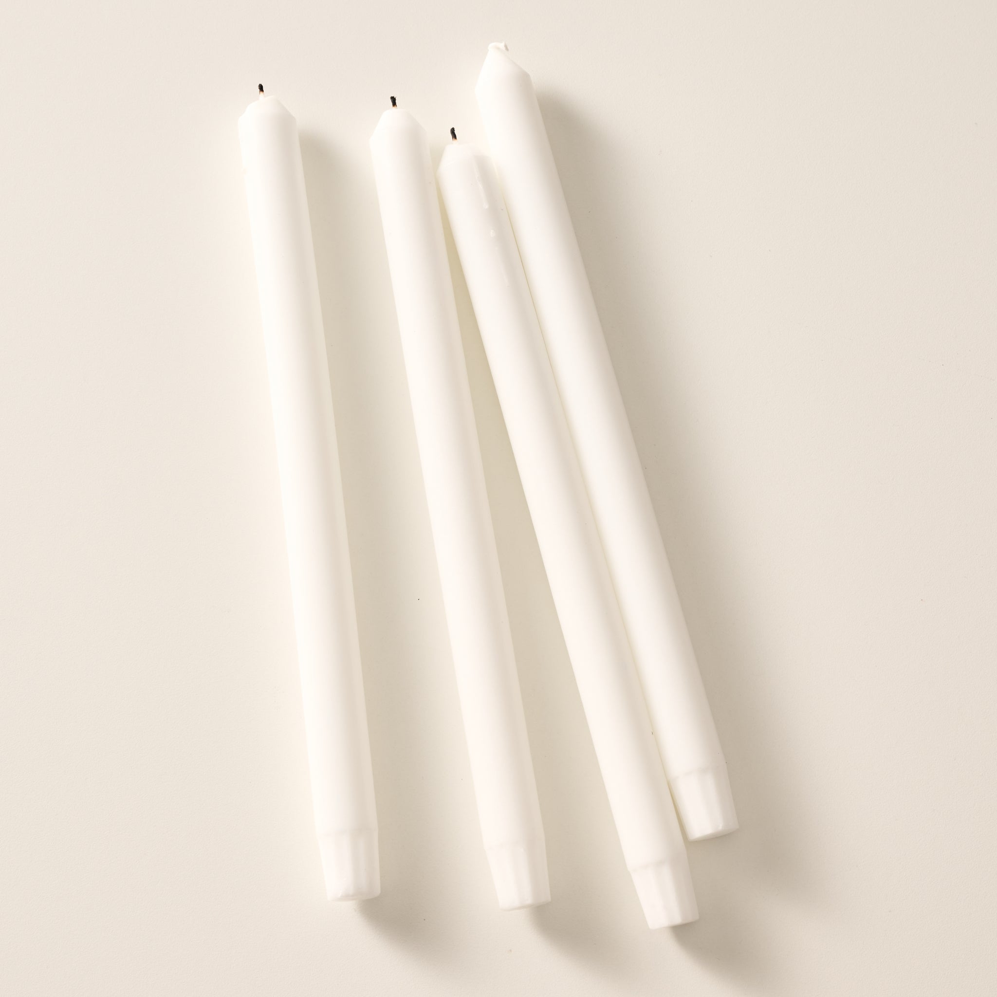 Four white taper candles, laying flat on a light beige background.