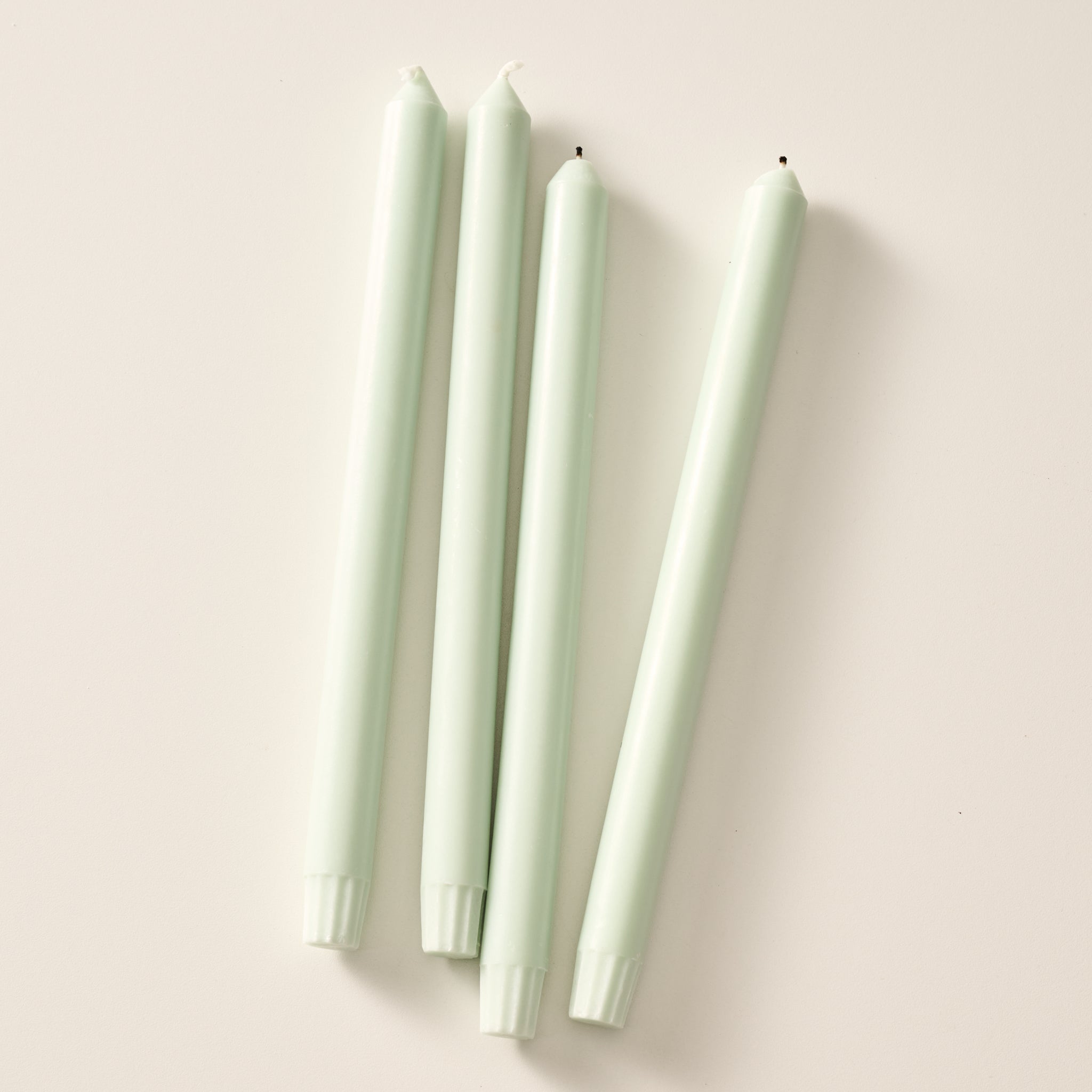 Four sage green taper candles laying flat on a light beige background.