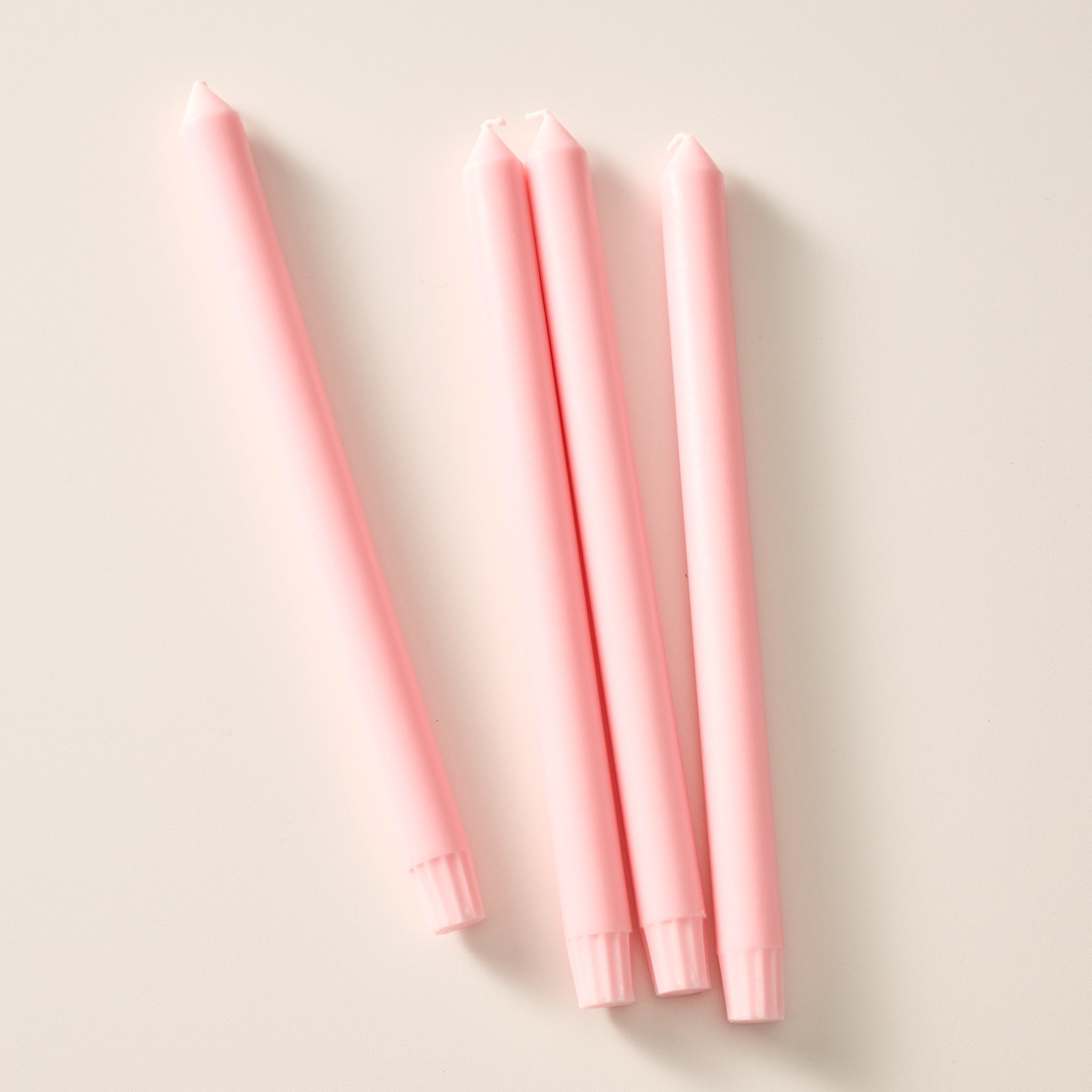 Four ginger colored taper candles laying flat on a light beige background.