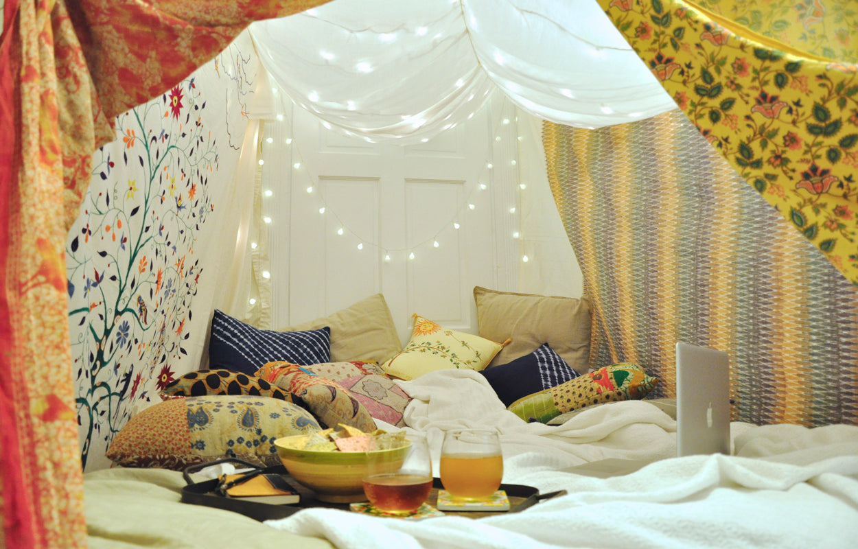 Blankets form a soft tent, with string lights draped in the background and pillows scattered around the floor.