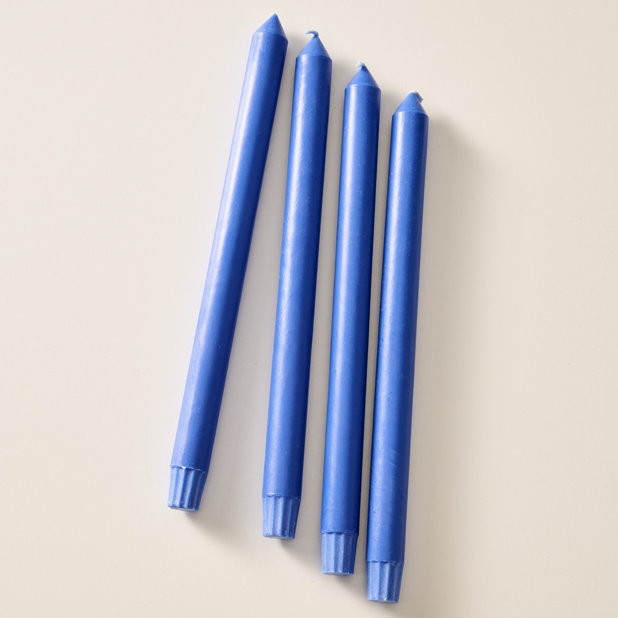 Four cobalt blue taper candles laying flat on a light beige background.